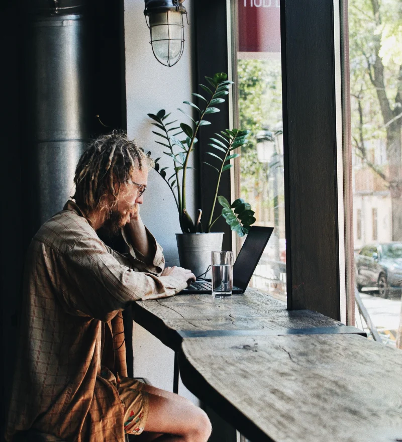 Kunden Onboarding automatisieren - junger Mann sitzt in einem Co Work Cafe an einem Tisch und arbeitet an seinem Laptop.